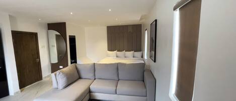 A modern hotel room with a large bed, a sofa, a wardrobe, and a mirror.