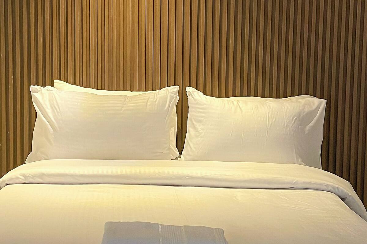 A hotel room with a large bed, two pillows, and a headboard with vertical lines.