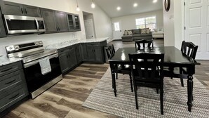 A modern kitchen with dark cabinetry, stainless steel appliances, and a dining area with a wooden table and chairs.
