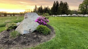 A landscaped garden with a large rock, a flower bed with pink flowers, and a well-maintained lawn.