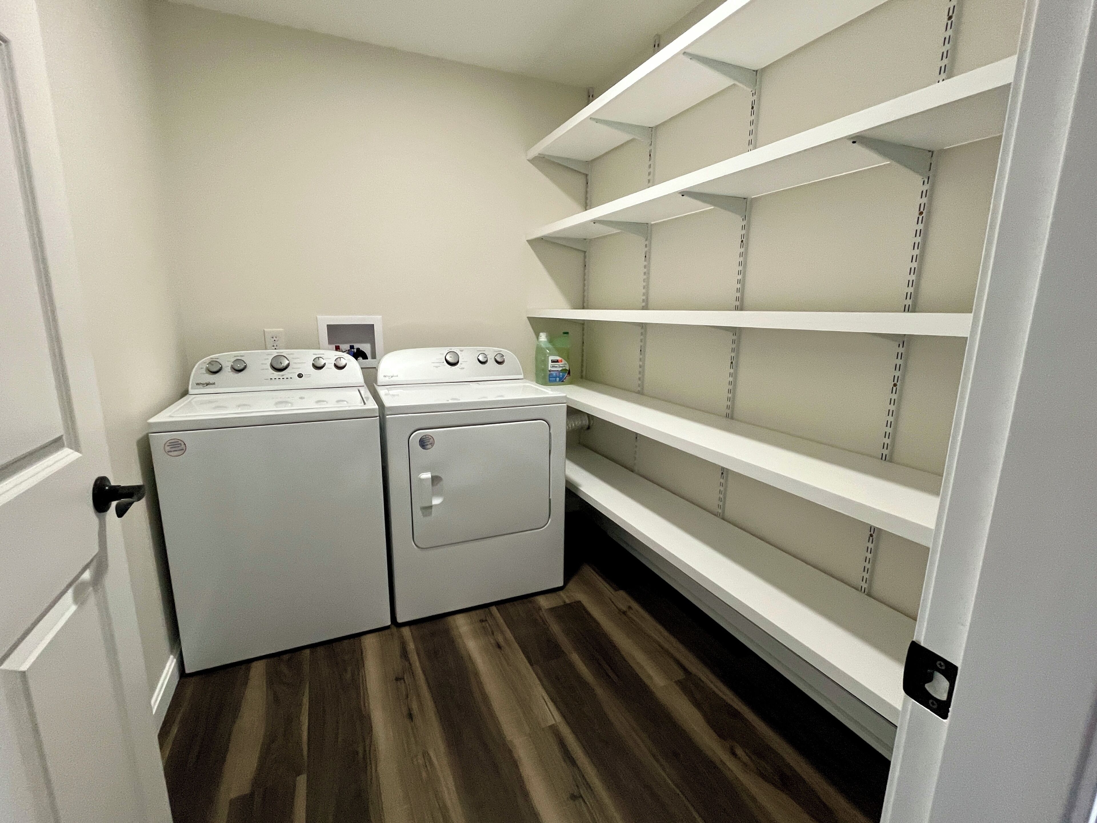 Une buanderie équipée de deux appareils lave-linge et sèche-linge superposés, d’une étagère avec une bouteille et d’une porte dotée d’une poignée.