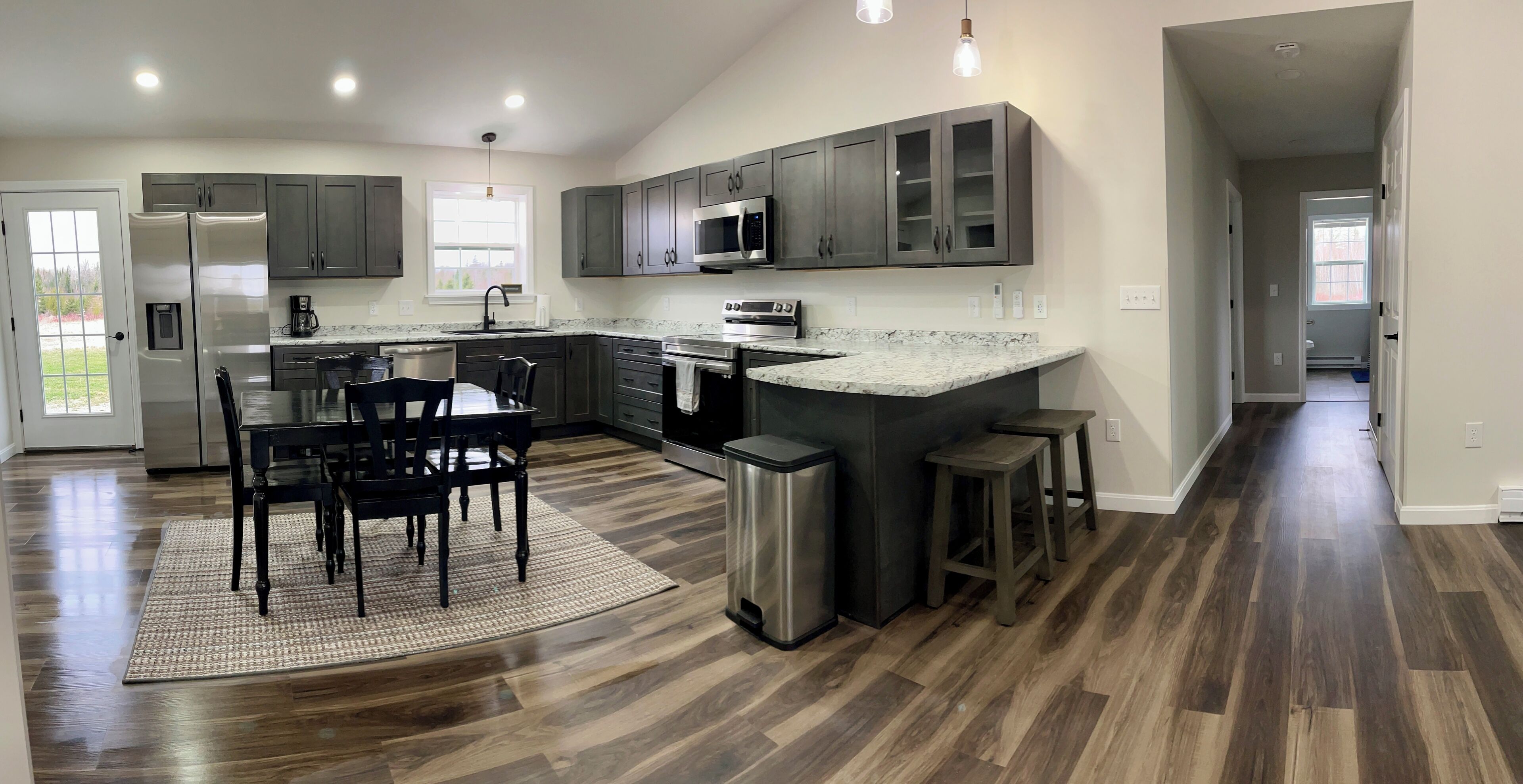 A modern kitchen with dark wood cabinets, a granite countertop, stainless steel appliances, and a dining area with a rug and chairs.
