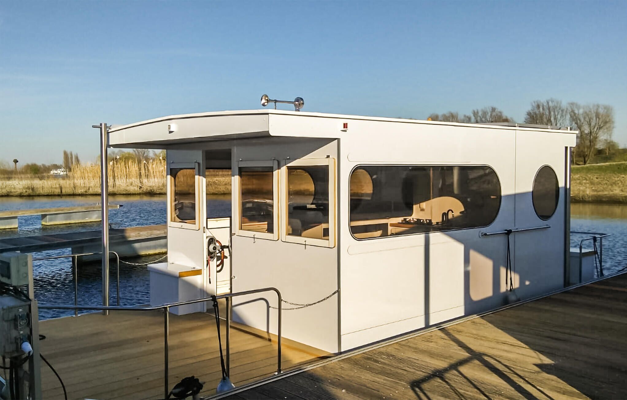 Une péniche à quai, dotée d’une terrasse couverte, de grandes fenêtres et d’un petit espace cabine.