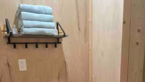 Ein kleines Badezimmer mit Holzwandverkleidung, einer weißen Toilette, einem Mülleimer und einem Regal mit gefalteten Handtüchern.