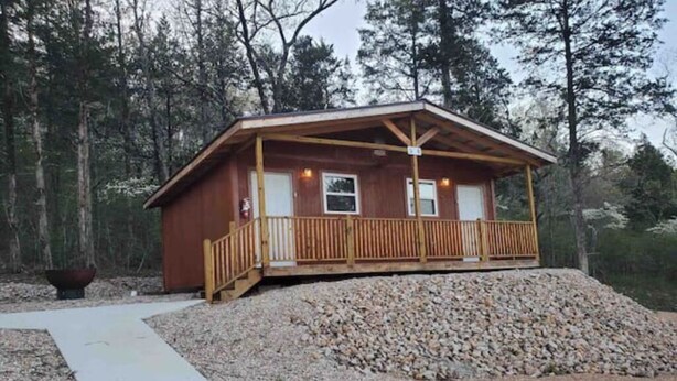 Eine Holzhütte mit einer Holzterrasse, einer überdachten Veranda und einem Schotterweg.