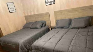 Zwei Einzelbetten mit grauer Bettwäsche in einem Zimmer mit Holzboden und einem hölzernen Kopfteil.