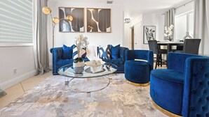 Een moderne woonkamer met blauwe banken, een glazen salontafel en abstracte wanddecoratie.