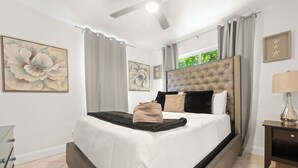 Een slaapkamer met een groot bed, een plafondventilator en een raam met gordijnen.