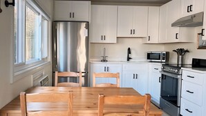 A modern kitchen with white cabinets, a stainless steel refrigerator, a microwave, an oven, and a dining table with wooden chairs. - Little Bell's Bungalow / Walkable to Saugatuck and Douglas / Updated (Saugatuck)