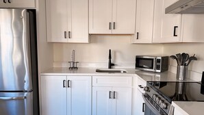 A modern kitchen with white cabinets, stainless steel appliances, a microwave, and a gas stove. - Little Bell's Bungalow / Walkable to Saugatuck and Douglas / Updated (Saugatuck)