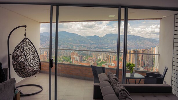 A balcony with a sofa, a hanging chair, and a table with a plant.
