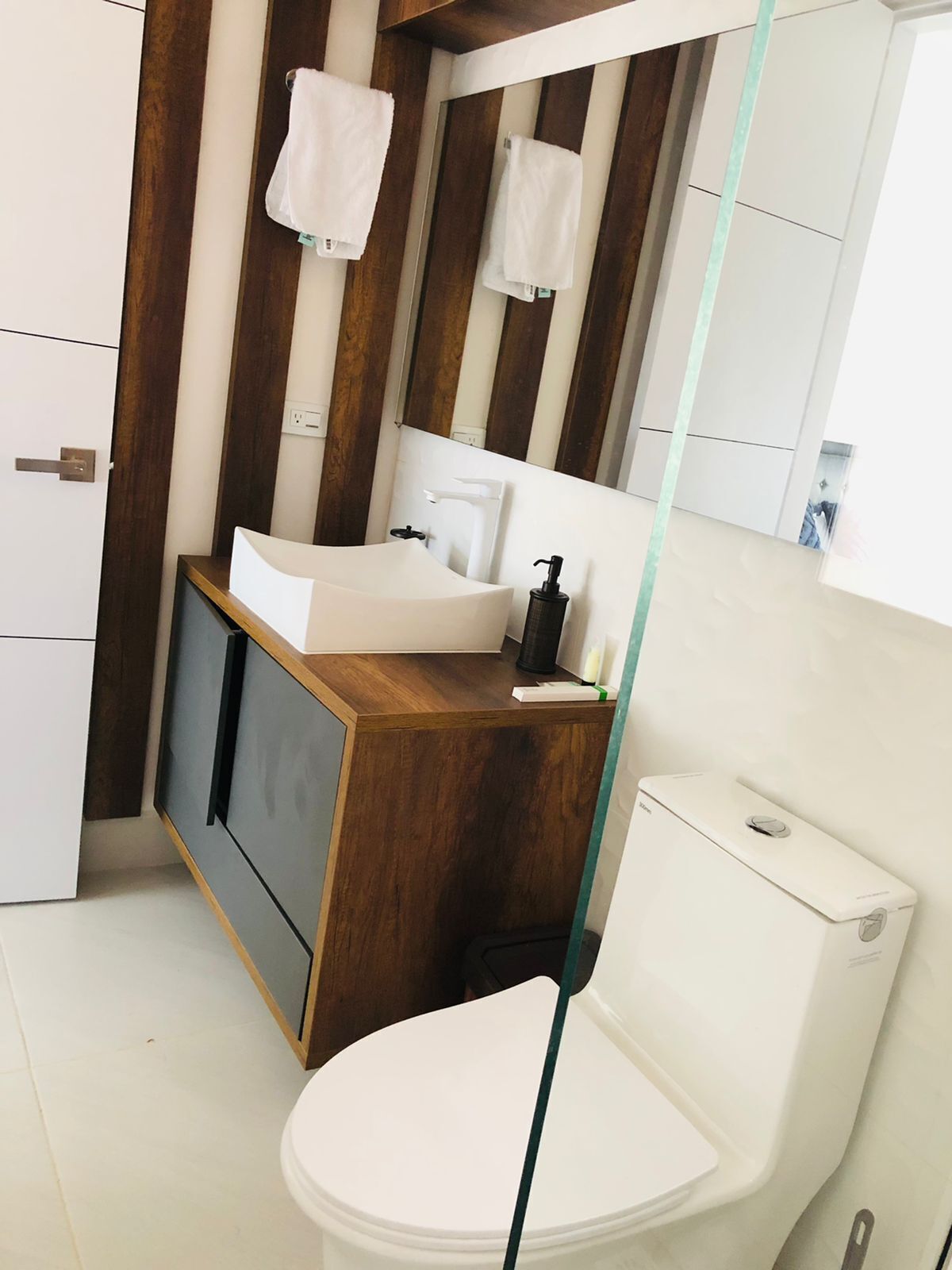 Une salle de bain moderne avec un meuble-lavabo en bois, un lavabo blanc, des toilettes et un miroir.