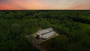 Um edifício moderno de dois andares com telhado plano, rodeado por vegetação densa.