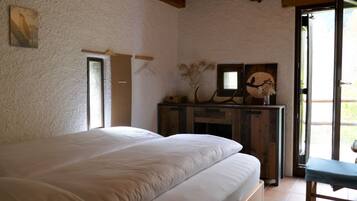 A bedroom with a large bed, wooden headboard, a dresser with decorative items, and a sliding glass door to the right.