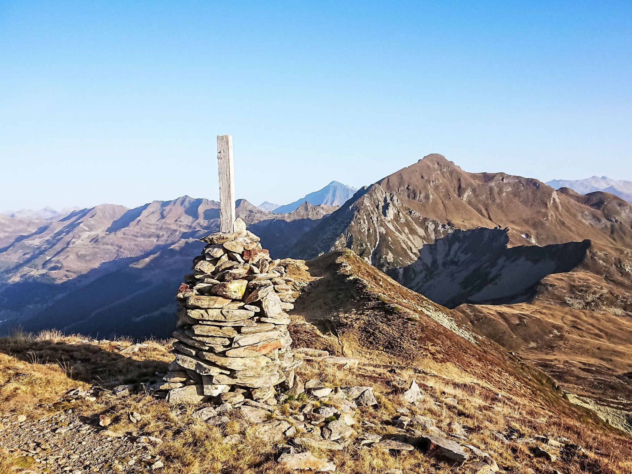 Un cairn de pierres, situé sur une crête montagneuse, d’où l’on a une vue dégagée sur les montagnes lointaines.