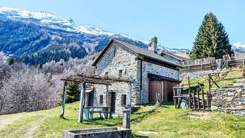 A stone building with a wooden pergola, a stone bench, and a view of snow-capped mountains.