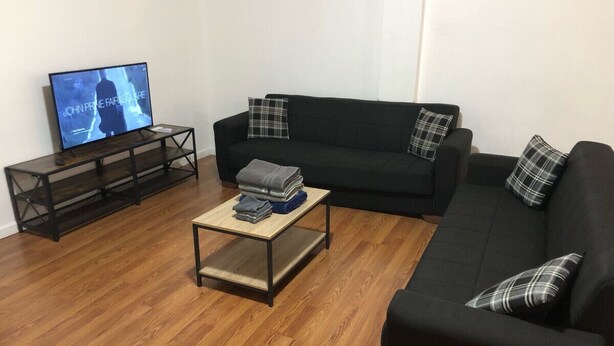A living room with a black sofa, a coffee table, a TV on a stand, and a plaid pillow.