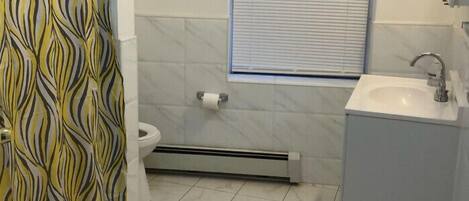Une salle de bain avec des toilettes, une fenêtre, un lavabo et un rideau de douche.