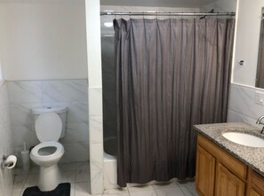A bathroom with a toilet, shower curtain, sink, and wooden cabinets. - Large apartment, direct NYC train 5 min walk, MetLife Stadium 30 mins (Elizabeth)