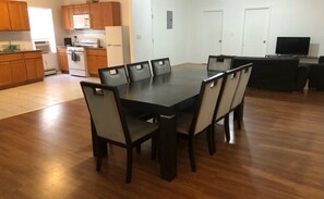 A modern kitchen with wooden cabinets, a dining table with chairs, and a flat-screen TV.