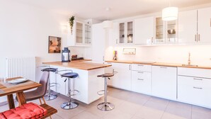 Una cocina moderna con armarios blancos, encimera de madera y taburetes de bar.