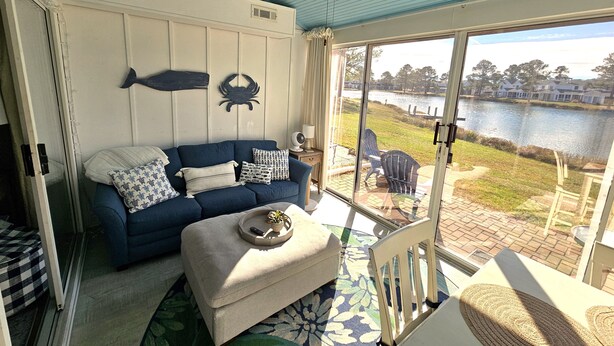 A room with a blue couch, a white ottoman, and a view of a lake through large glass doors. - Lovely Mallard Lakes townhome, minutes from Fenwick and OC beaches. (Selbyville)
