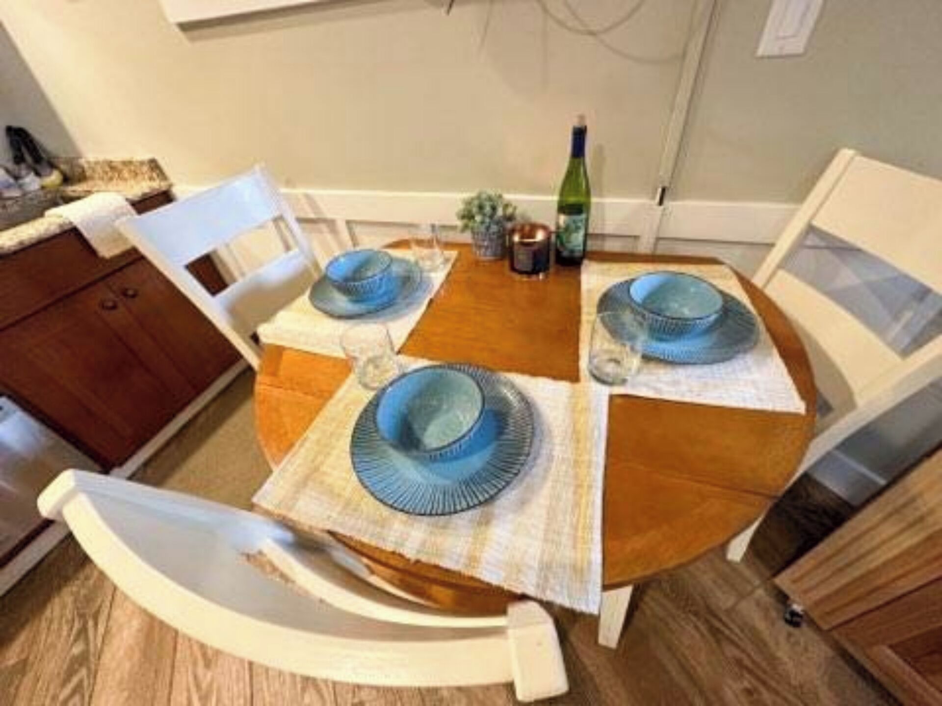 A dining table set with blue plates and glasses, surrounded by white chairs.