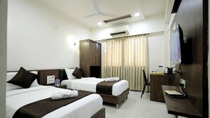 A hotel room with two beds, a desk, a chair, an air conditioning unit, a ceiling fan, and a television. - Hotel A1 Plaza - Ahmedabad (Ahmedabad)