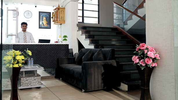 A reception area with a reception desk, a black sofa, a staircase, and a vase with flowers. - Hotel A1 Plaza - Ahmedabad (Ahmedabad)