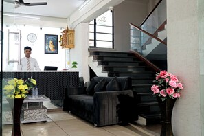 Ein Empfangsbereich mit Empfangstresen, einem schwarzen Sofa, einer Treppe und einer Vase mit Blumen.