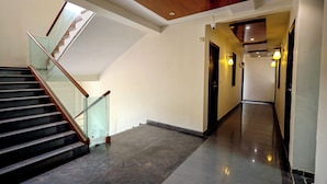 A modern interior with a staircase, a hallway, and a polished floor. - Hotel A1 Plaza - Ahmedabad (Ahmedabad)