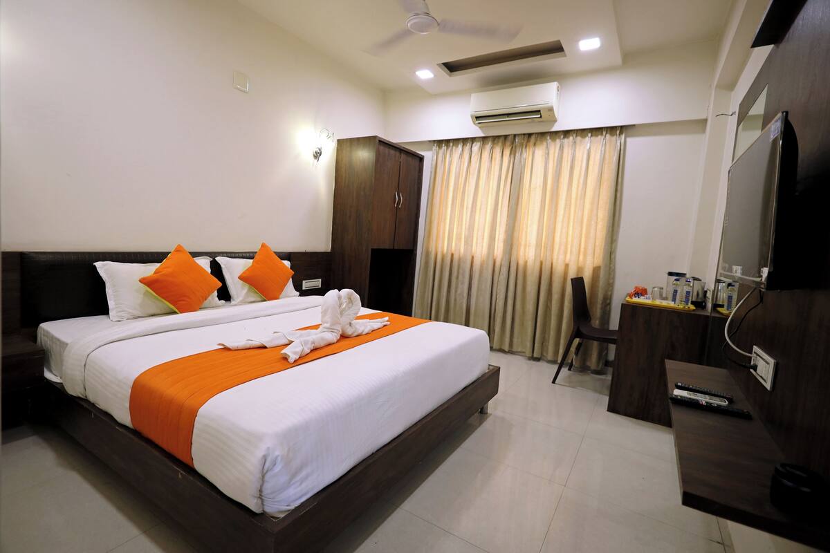 A hotel room with a large bed, a desk, a chair, an air conditioning unit, and a television.