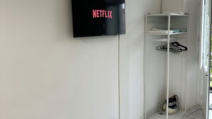 Une pièce avec un téléviseur fixé au mur qui affiche le logo « NETFLIX », une armoire blanche et un tapis à motifs.