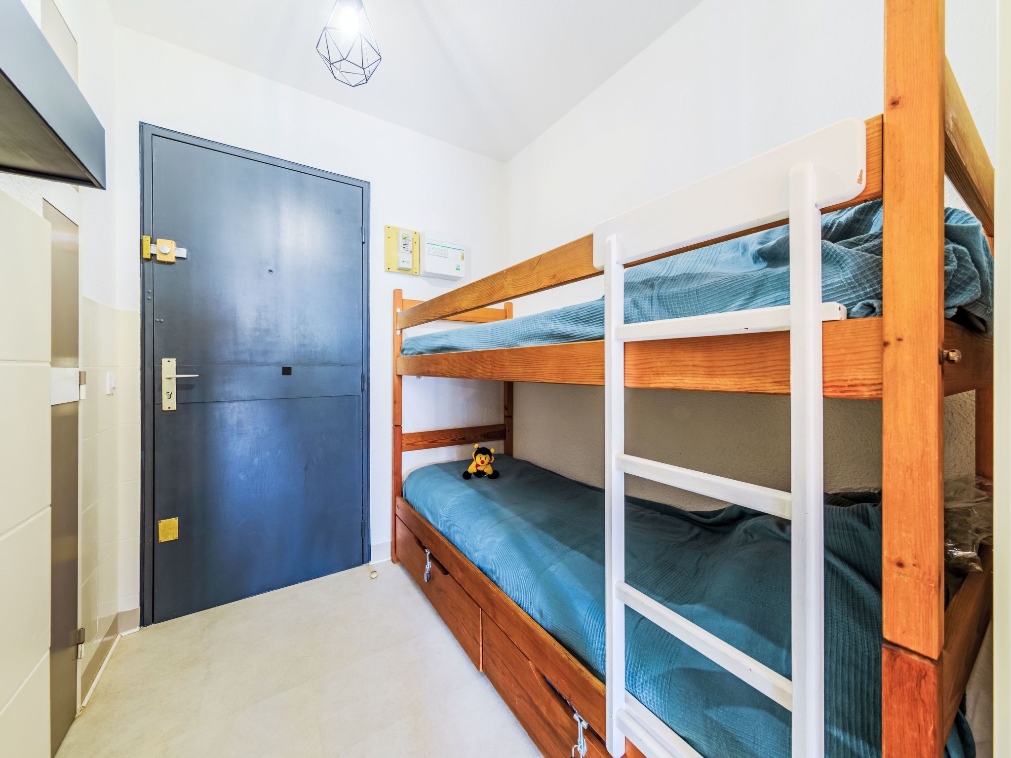A small, compact room with a bunk bed, a door, and a light fixture.