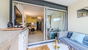 Una cocina moderna con gabinetes amarillos, un comedor con una mesa y sillas, y un balcón con un sofá y una mesa con una botella y vasos.