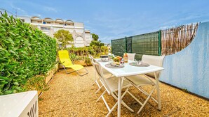 Un patio al aire libre con una mesa y sillas blancas, rodeado de follaje y una pared azul.