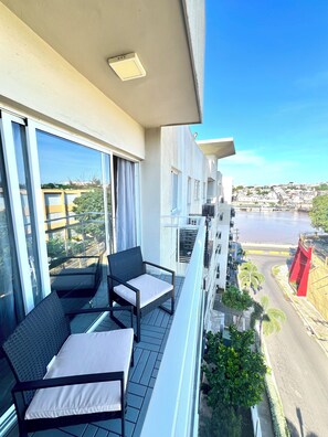 A balcony with two chairs and a table, overlooking a river and a cityscape.