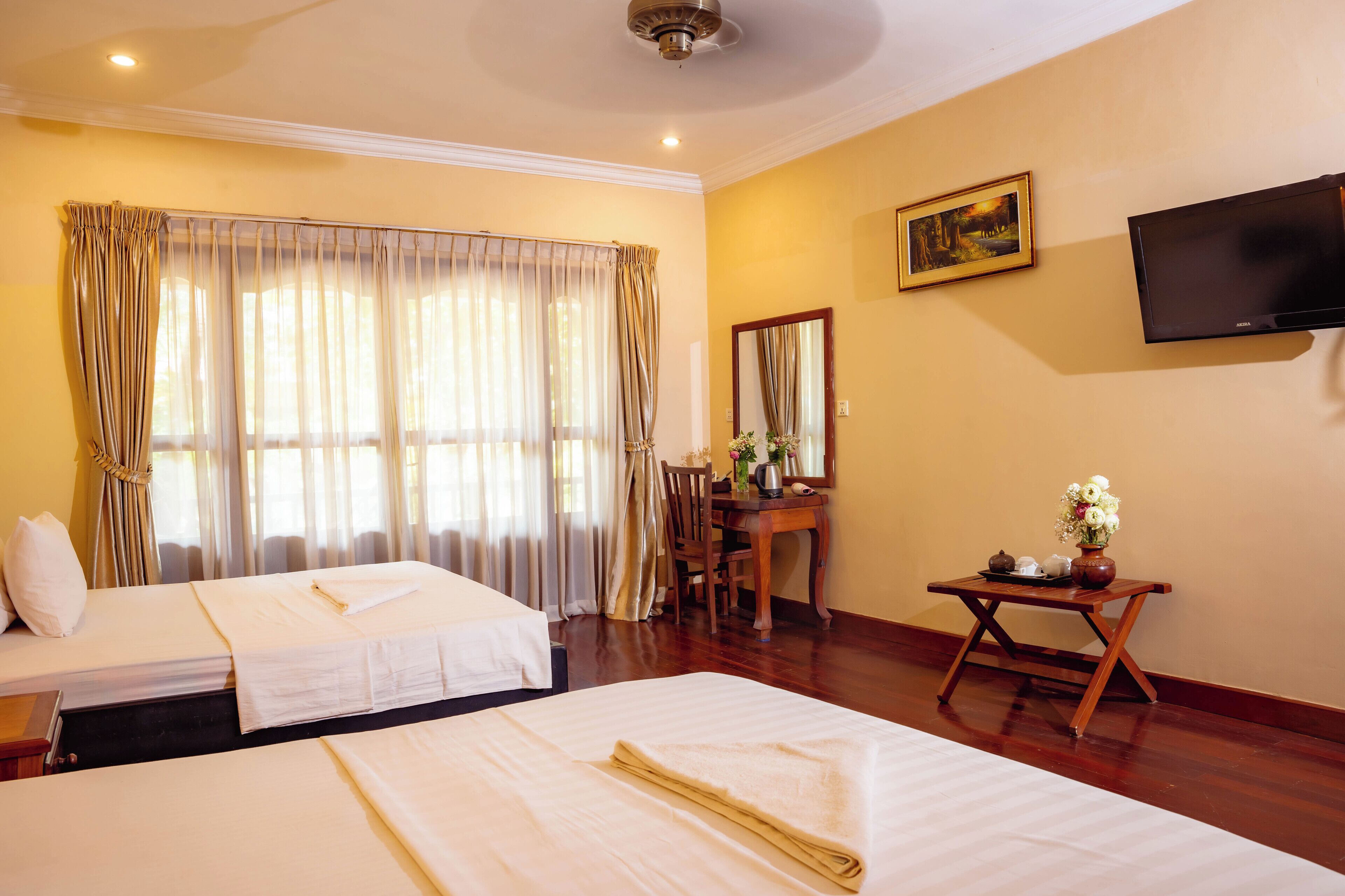 Une chambre d’hôtel avec deux lits, un bureau avec une chaise, un téléviseur fixé au mur et un tableau.