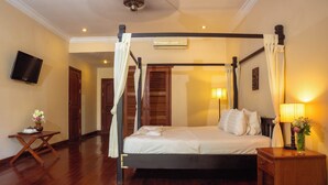 Una cama con dosel y cuatro columnas, una mesita de noche con lámpara, y un televisor fijado en la pared.