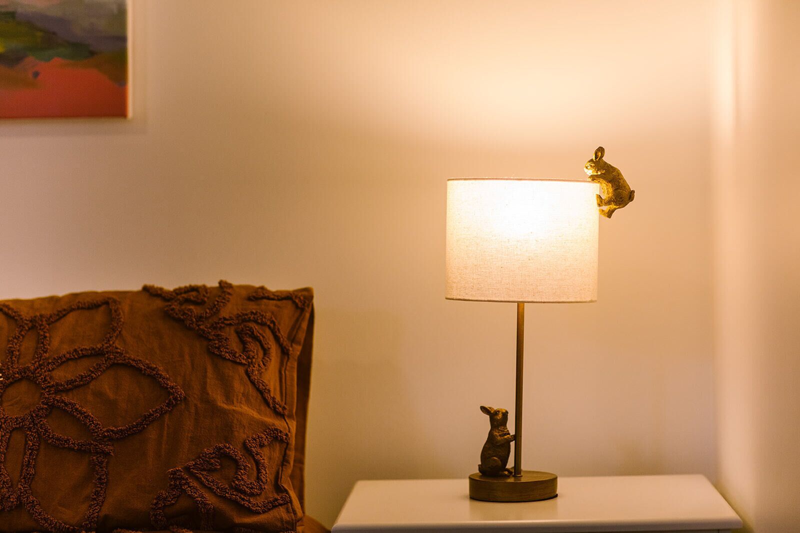 A bedside table with a lamp featuring a rabbit figurine and a white lampshade.