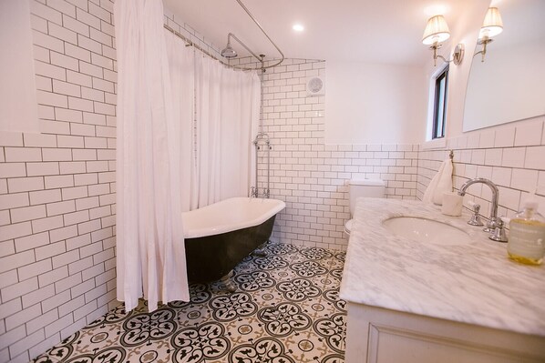 A bathroom with a black bathtub, white tiled walls, a patterned floor, and a white vanity with a mirror and two lights.