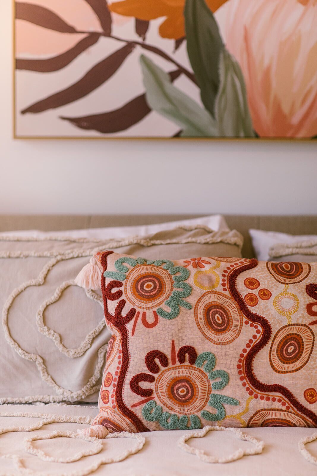 A bed with a patterned pillow and a painting of flowers on the wall.