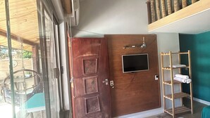 Una habitación con una cama, un televisor montado en la pared, un ventilador de techo y una puerta de madera.