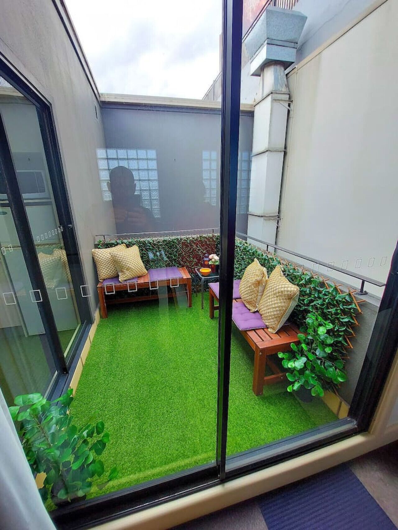 Un pequeño espacio al aire libre con césped artificial verde, muebles de madera y plantas en macetas.