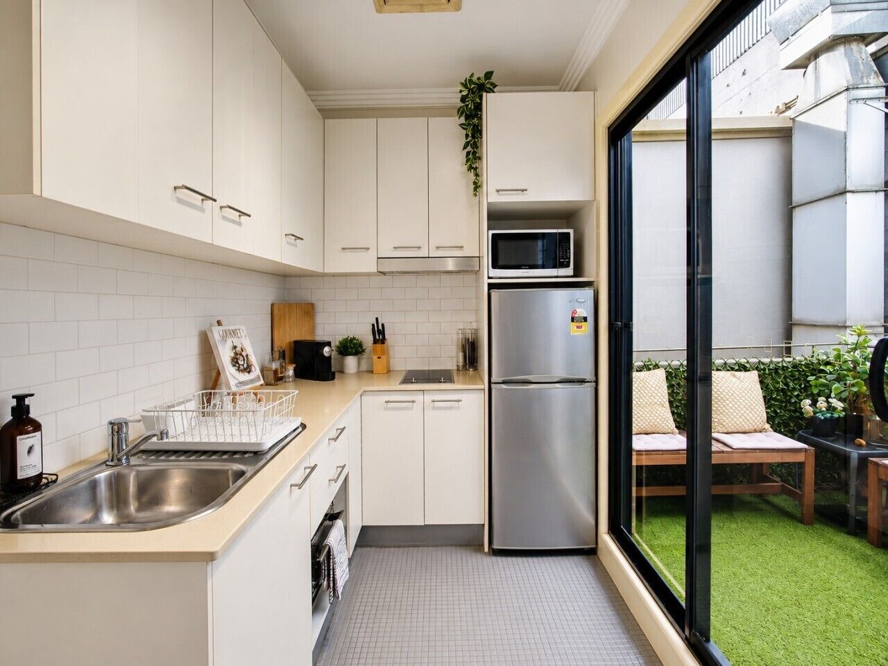A compact kitchen with white cabinets, a stainless steel refrigerator, a microwave, and a sink.