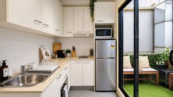 A compact kitchen with white cabinets, a stainless steel refrigerator, a microwave, and a sink.