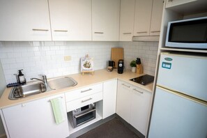 Una cocina compacta con armarios blancos, un lavamanos de acero inoxidable, un microondas y un horno empotrado.