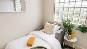 A bedroom with a bed, a bedside table with a plant, a window with blinds, and a mirror on the wall. - Great apartment in the City / Broadway-Chippendale, Sydney (Chippendale)