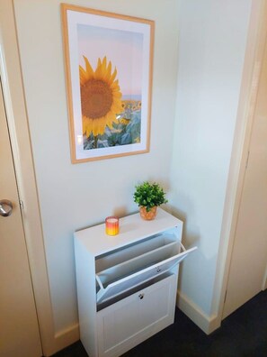 A hallway with a white cabinet, a framed sunflower picture, a small potted plant, and a candle.