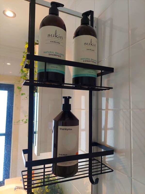 A bathroom shelf with three bottles of Sukun haircare products and one bottle of Thankyou body wash.